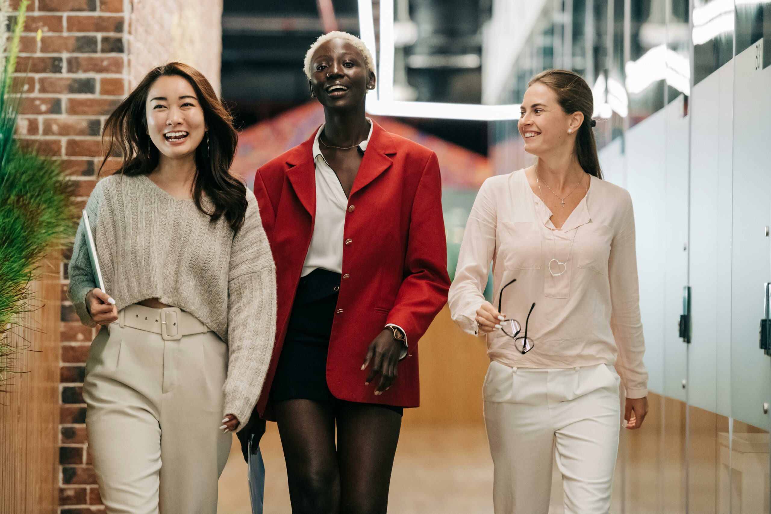 Three women walking through an office corridor, engaged in a lively conversation.