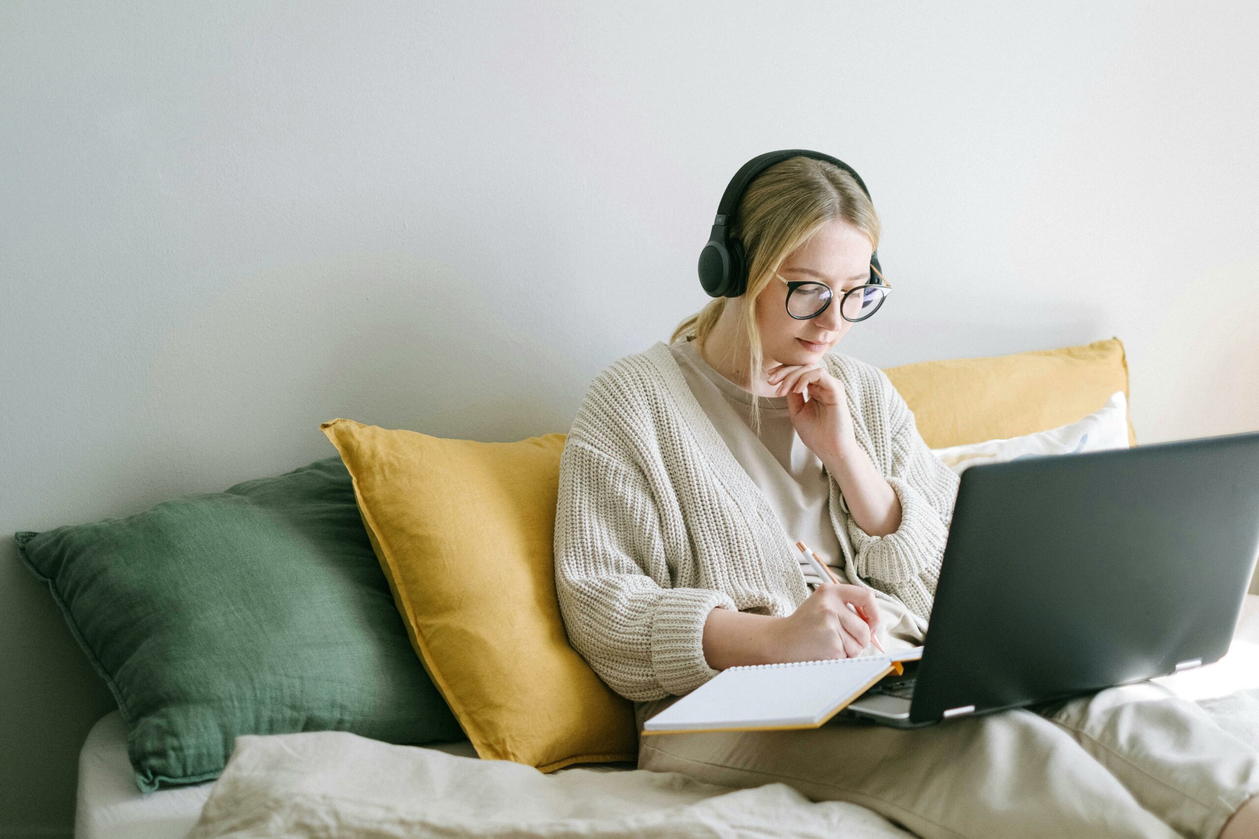 A woman is working from home, wearing headphones as she works on her laptop.